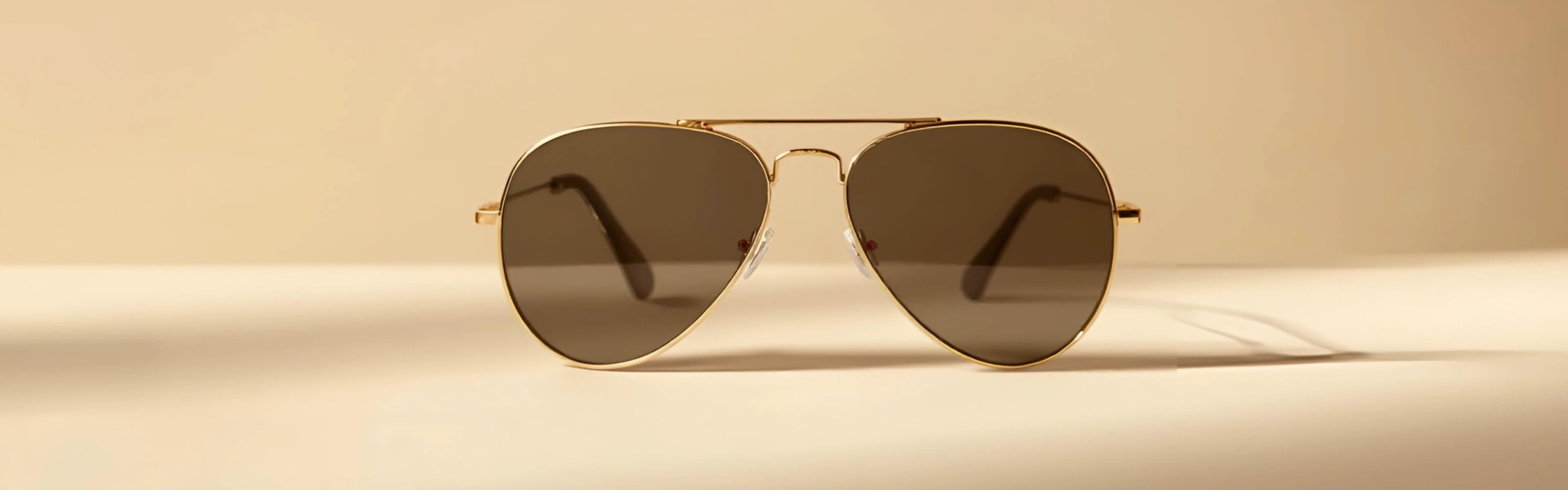 Aviator sunglasses with gold frame and dark lenses on a beige background
